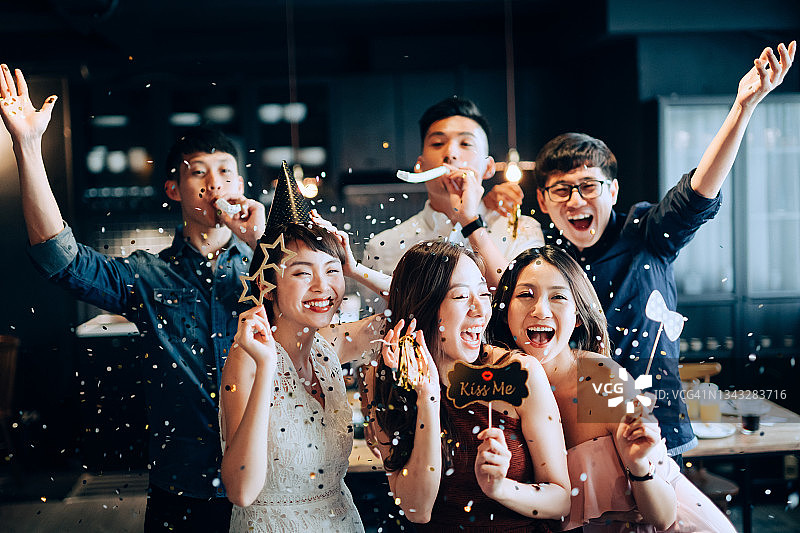 一群快乐的亚洲男人和女人在派对上玩道具和吹闪闪发光的五彩纸屑图片素材