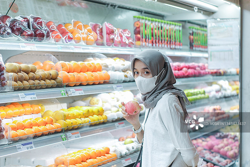 亚洲年轻女子戴着口罩在超市买水果图片素材