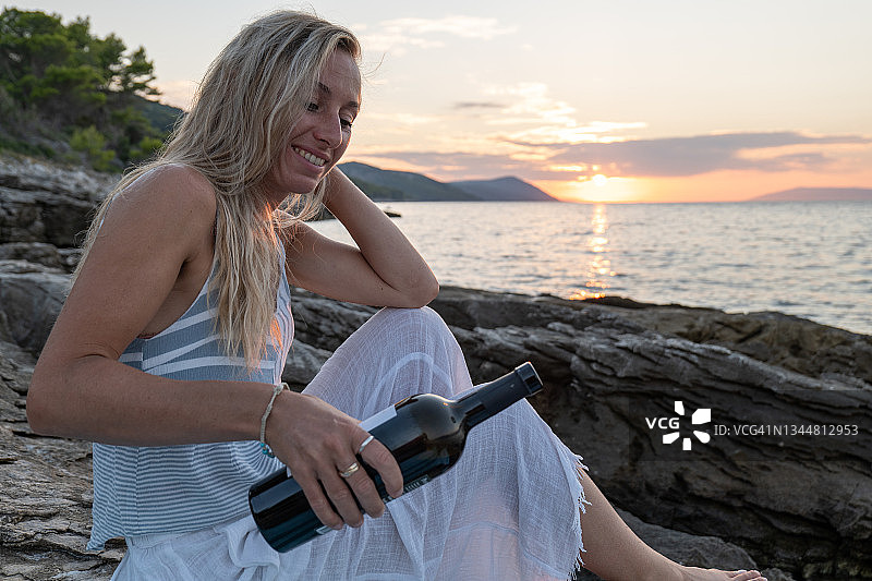 日落时分，一个年轻女子在海边喝红酒图片素材
