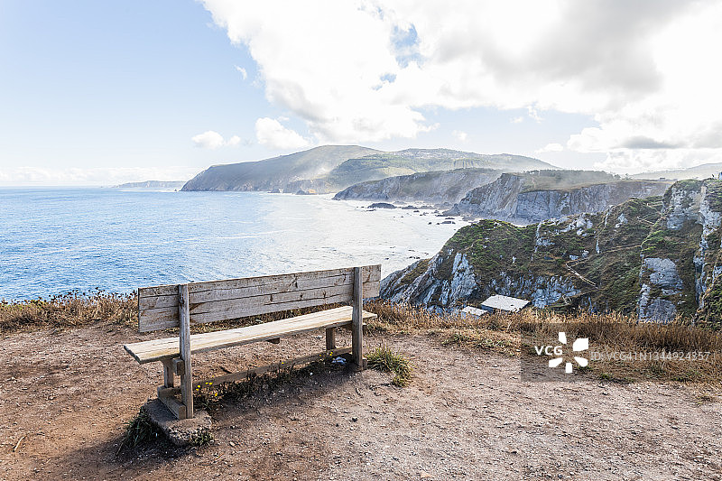 古老的木凳位于悬崖附近的海湾与岩石山在阳光明媚的日子与多云的天空在西班牙图片素材