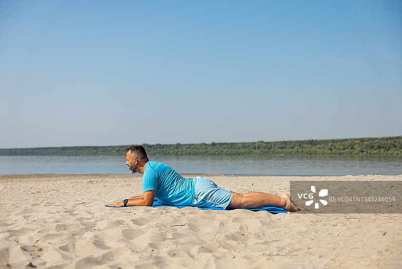 在一个晴朗的日子里，一名男子在海滩上做眼镜蛇瑜伽图片素材