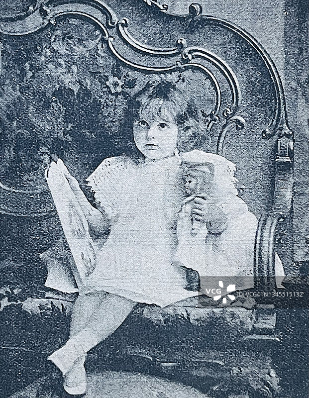 女孩坐在沙发上，手里拿着一个洋娃娃和她的图画书图片素材