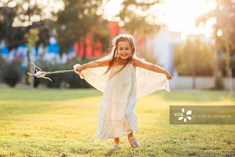 小女孩穿着仙女的衣服，拿着魔杖，在绿草地上昂首阔步图片素材