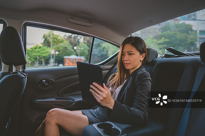 美丽的亚洲女企业家坐在车里用数字平板电脑工作图片素材