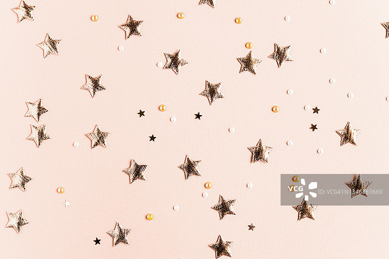 在纯色的米色背景上点缀着金色的星星和闪闪发光的节日背景。明亮的明信片为圣诞节，新年，晚会与闪亮和明亮的装饰。图片素材