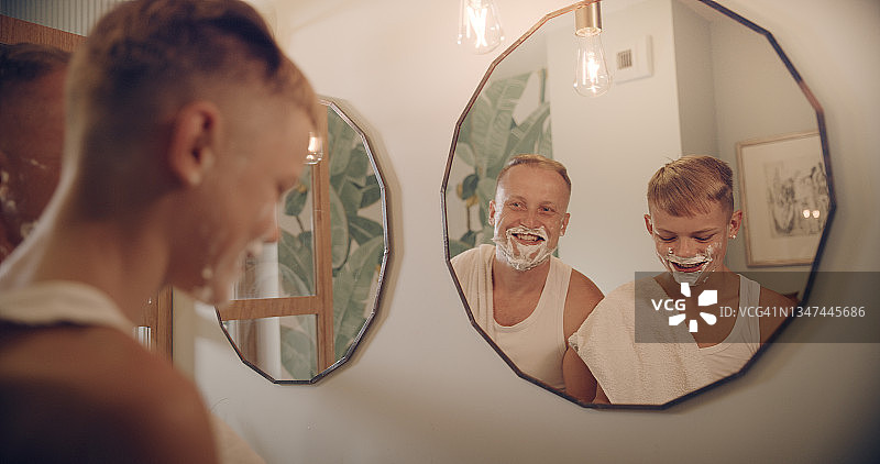 父亲和儿子在享受刮胡子的乐趣。和孩子共度美好时光。镜面反射图片素材