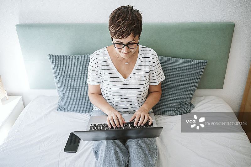 一个短发女人坐在家里的床上用笔记本电脑图片素材