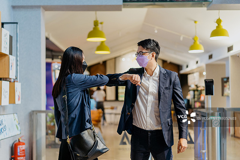 亚洲商人和女商人戴着防护口罩在办公室碰肘图片素材