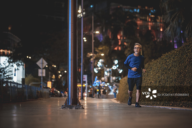 亚洲华人老人晚上独自在城市里跑步慢跑图片素材