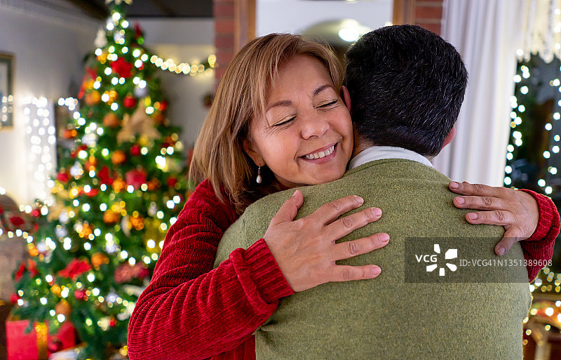 幸福和爱的女人在圣诞节闭着眼睛拥抱她的丈夫图片素材