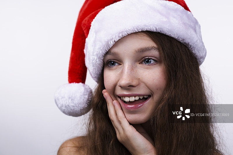 一个美丽可爱的牙齿微笑的年轻女子的肖像穿着圣诞老人的帽子在白色的背景图片素材