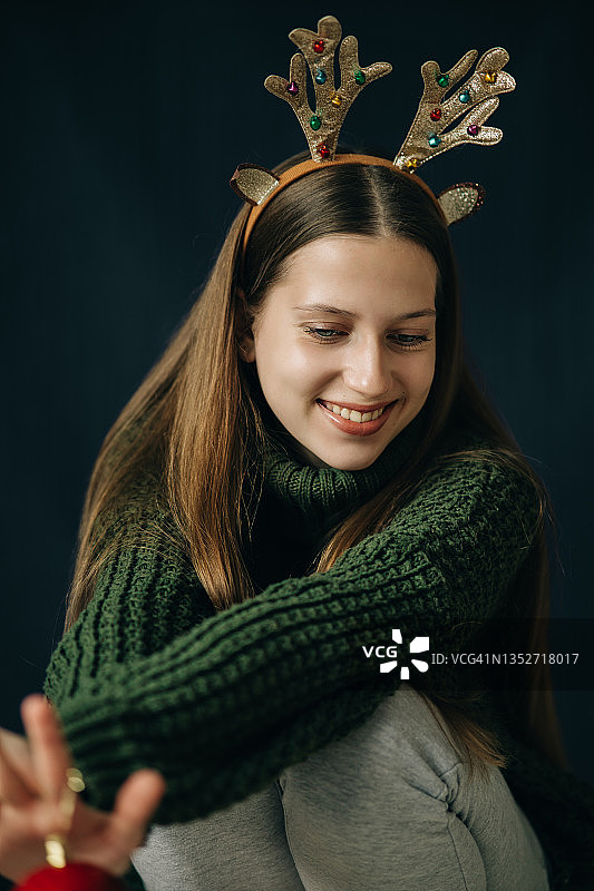 十几岁的女孩带着圣诞鹿角穿着绿色毛衣，面带微笑图片素材