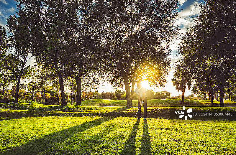 一名男子在风景如画的阳光明媚的高尔夫球场上开球，挥舞着太阳耀斑图片素材