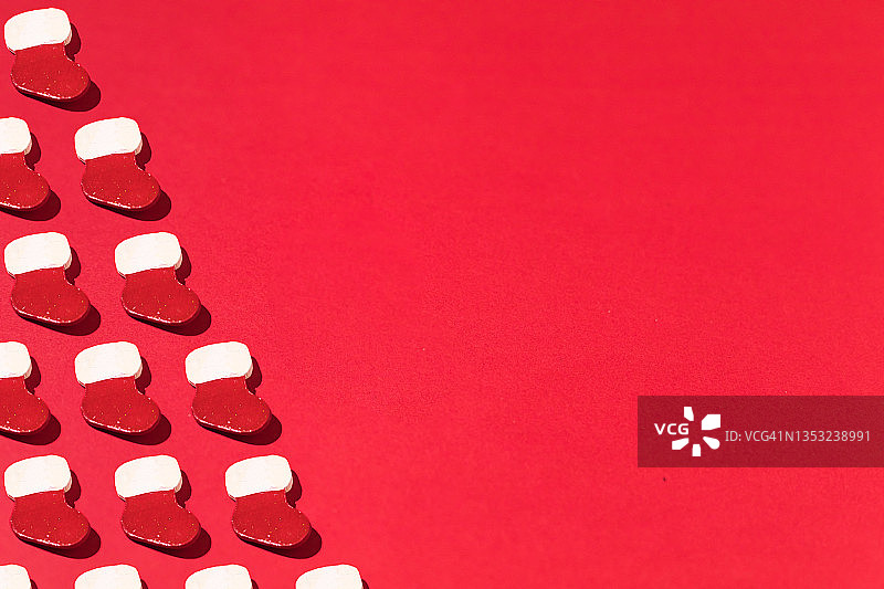 红色和白色圣诞老人的圣诞靴和袜子图案与硬阴影，在左侧与复制空间，在红色背景。圣诞节、冬天和下雪的概念。图片素材