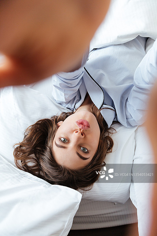 穿着睡衣的微笑女孩躺在床上自拍图片素材