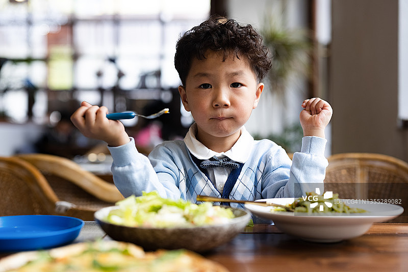 一个小男孩正在餐馆里吃意大利面和沙拉图片素材