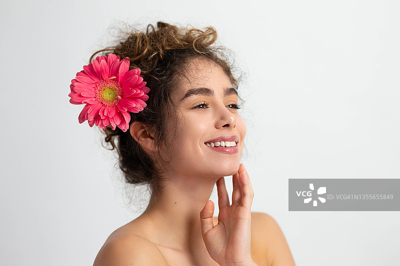 一个迷人的微笑着的女人，头发上插着一朵花，面部皮肤干净、健康图片素材