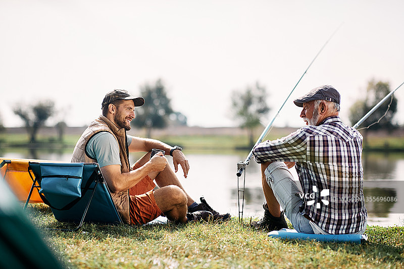 老人和他已成年的儿子在河边钓鱼时聊天。图片素材