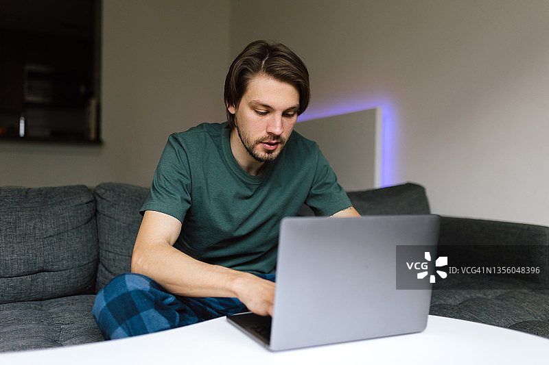 一个年轻人一边在家工作一边用笔记本电脑打字图片素材