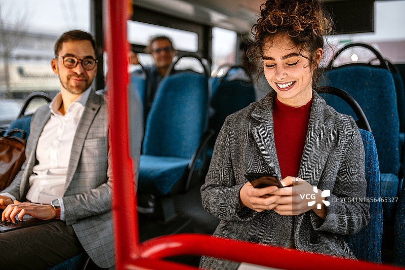 微笑的女人在乘公共汽车旅行时使用手机图片素材