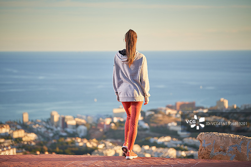 长头发和红色打底裤的运动女人从山上看着大海图片素材