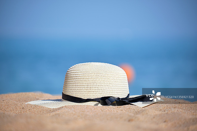 在温暖的阳光明媚的日子里，黄色草帽在热带海滨的沙滩上的特写。暑假的概念。图片素材