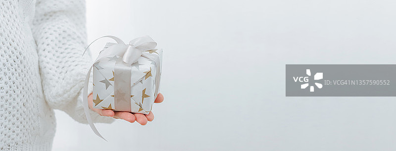 女性手捧着小礼品盒。寒假概念新年圣诞节。选择性对焦，浅色背景图片素材