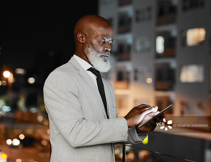 一个成熟的商人晚上站在办公室外使用平板电脑图片素材
