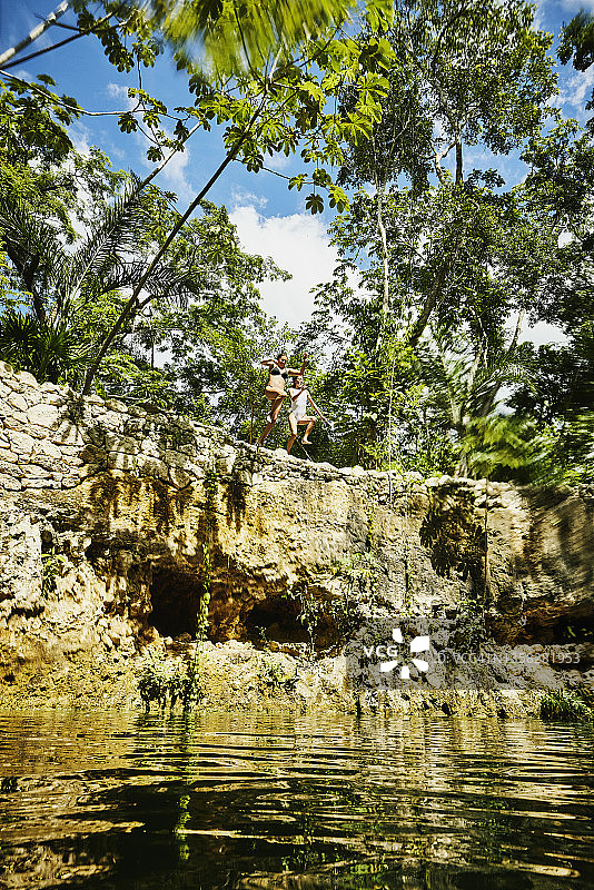 在丛林生态度假村，女性朋友们从平台上跳入天然井的广角镜头图片素材