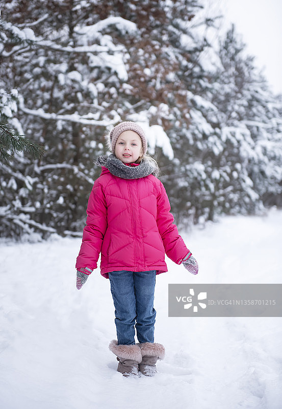 一个穿着鲜艳夹克的小女孩在冬天的森林里玩耍图片素材