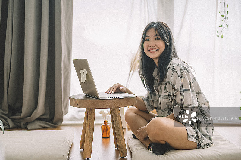 一位亚洲女学生坐在沙发上，带着笔记本电脑和笔记在客厅学习图片素材