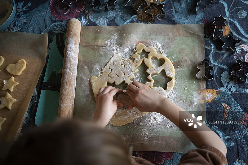 孩子们在餐桌上用饼干切割器把卷好的饼干面团切成圣诞节的形状。图片素材