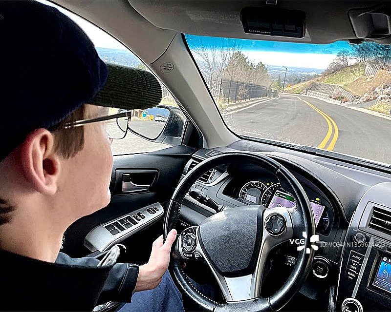 从车里看到的年轻成年男性在休闲服装驾驶下弯曲的双车道公路-股票照片图片素材