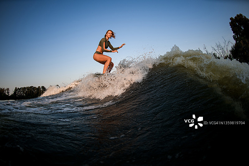 年轻的女冲浪者在碧蓝的天空下沿着河波冲下。图片素材