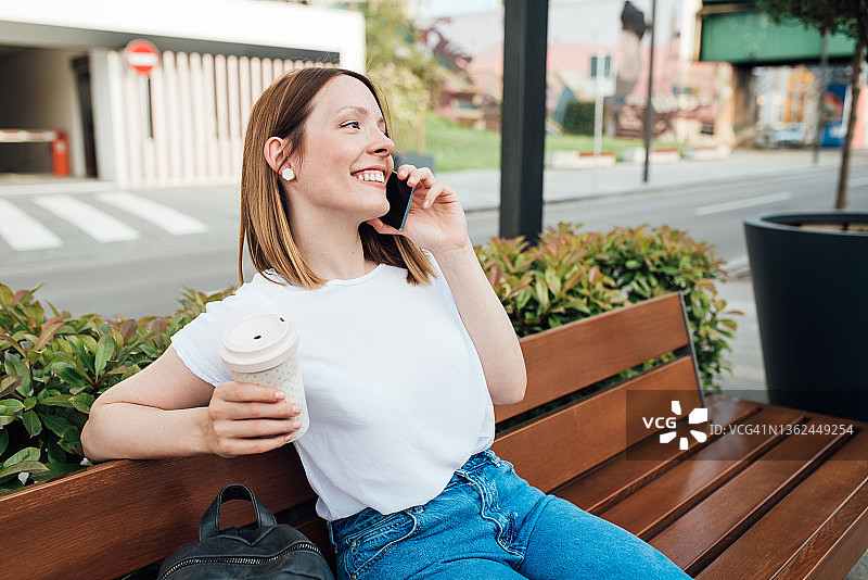 一个快乐的女孩享受咖啡和在街上讲手机的肖像图片素材