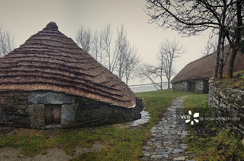 在多雨多雾的冬天，传统的茅草屋顶的石头房子。O Cebreiro村的加利西亚民族建筑，位于历史悠久的圣詹姆斯大道上图片素材