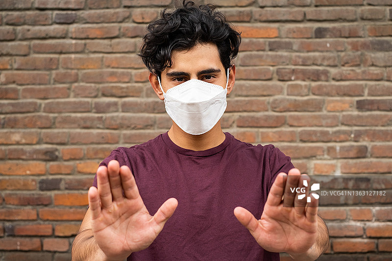 一个年轻的拉丁裔男子戴着口罩，看着镜头，示意停止图片素材