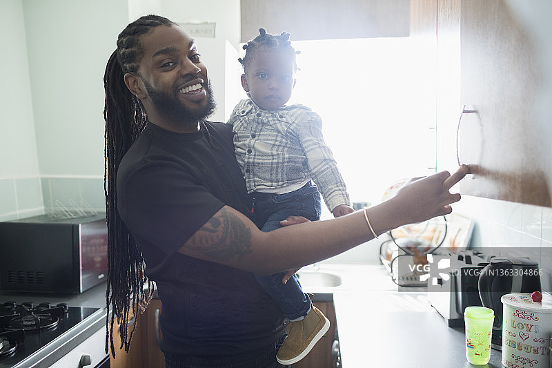 肖像快乐的父亲抱着蹒跚学步的儿子在公寓厨房图片素材