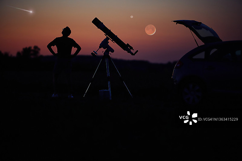 一个人的剪影，汽车，望远镜和乡村在星空下。图片素材