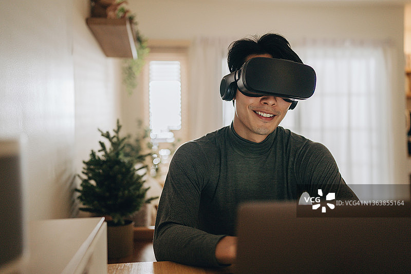 亚洲男人在家带着VR眼镜工作。图片素材