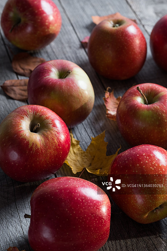 红色的苹果和秋天落下的黄叶桦树，枫树和白杨在木制的背景上。厨房桌子上的水果。有机农产品的种植。素食的概念，纯素，生食和饮食。秋天的自然背景。收割。图片素材