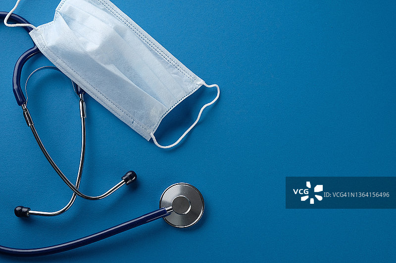 蓝色背景的一次性医用口罩和听诊器。医疗保健和医学的概念。图片素材