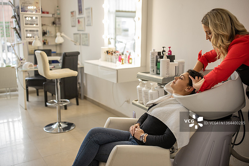 白人女性美发师在现代美发沙龙给客户洗头发图片素材