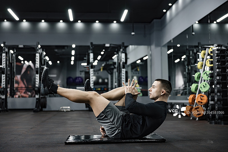 一个健康的运动员坐在体育馆的垫子上做热身运动。图片素材
