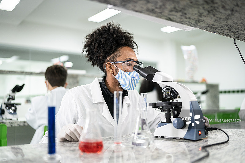 一个年轻人在实验室里用显微镜，戴着口罩图片素材