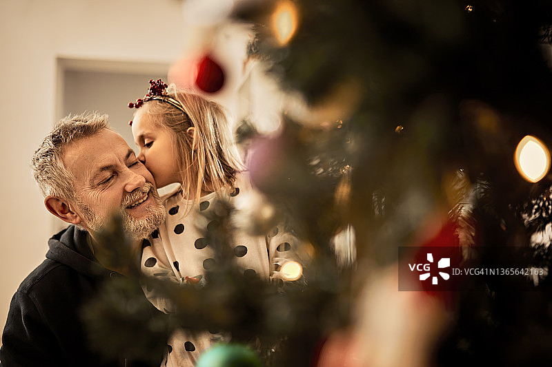 孙女在家里的圣诞树后面亲吻爷爷图片素材