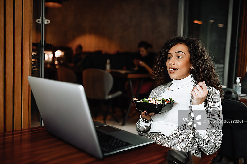 女性在吃沙拉的午餐时间用笔记本电脑开视频会议图片素材