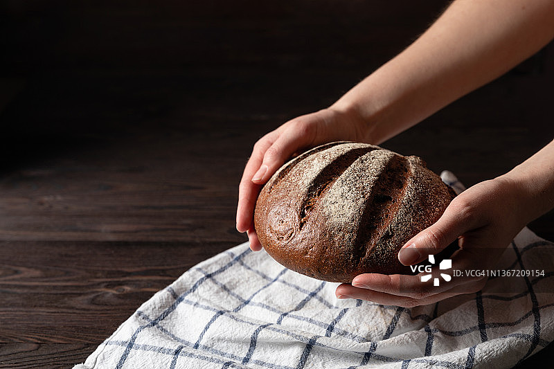 木制背景的自制硬皮面包。面包师手里拿着新鲜的面包。图片素材