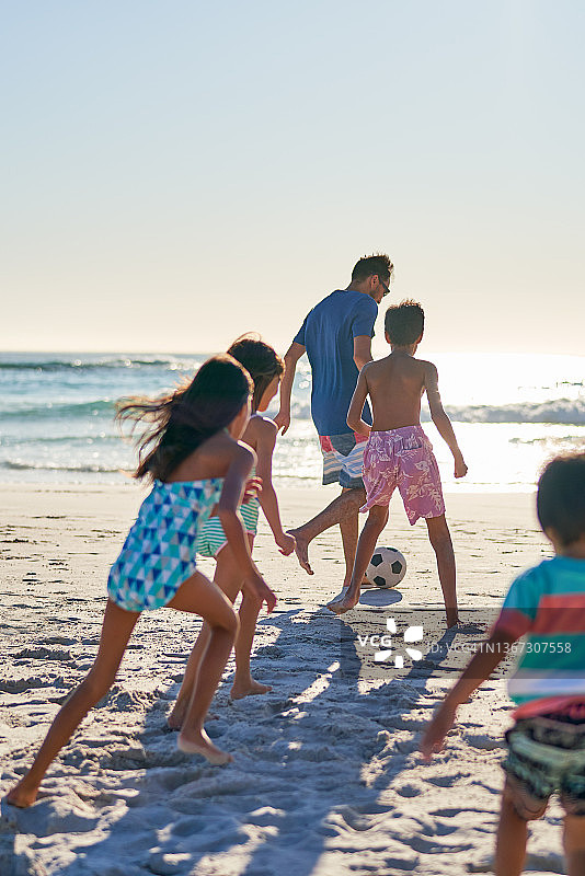 一家人在阳光明媚的海滩上踢足球图片素材