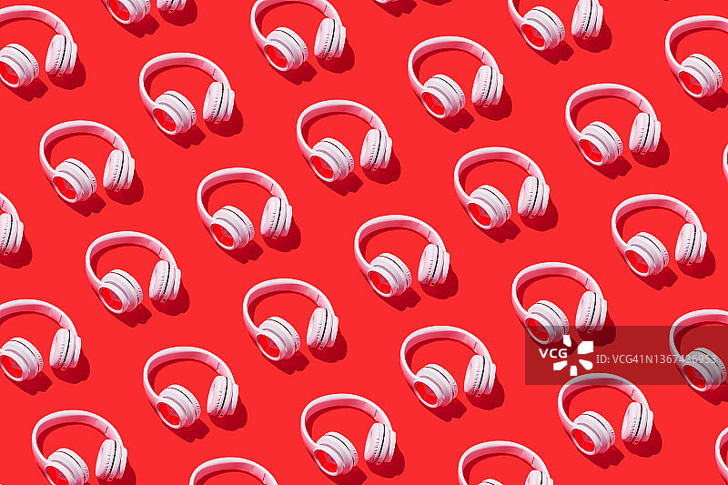 白色无线耳机的图案与红色背景上的硬阴影。概念音乐，耳机，收音机，播客，听和放松活动。图片素材